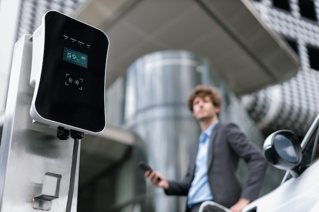 Progressive businessman with EV car at public parking car charging station