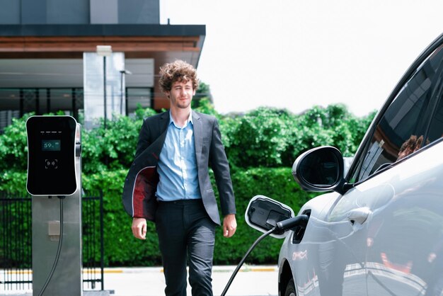 Progressive businessman with EV car at public parking car charging station