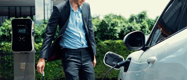 Progressive businessman with EV car at public parking car charging station