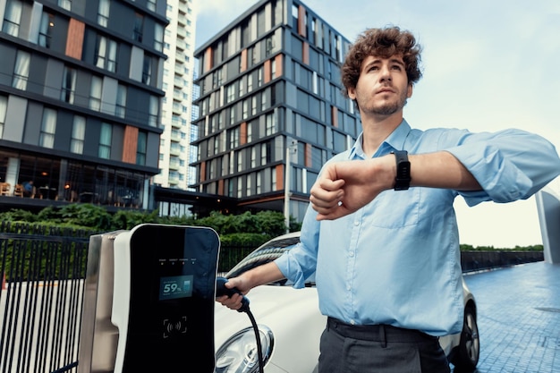 Progressive businessman with smartwatch at public charging station for EV car