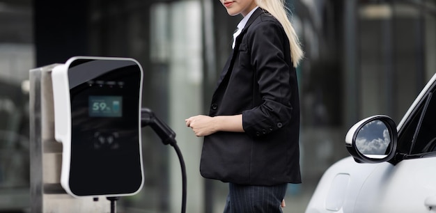 Progressive businesswoman plugs charger plug from charging station to EV