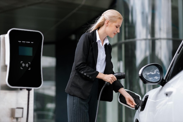 Progressive businesswoman plugs charger plug from charging station to EV