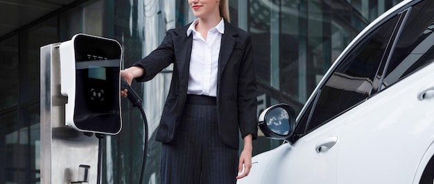 Progressive businesswoman with EV car at public parking car charging station