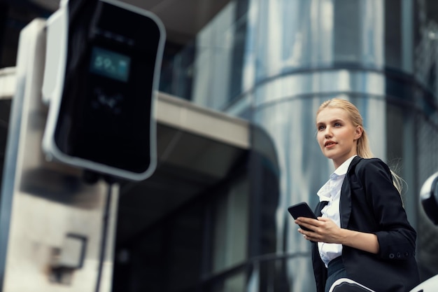 Progressive businesswoman with mockup smartphone with EV at charging station