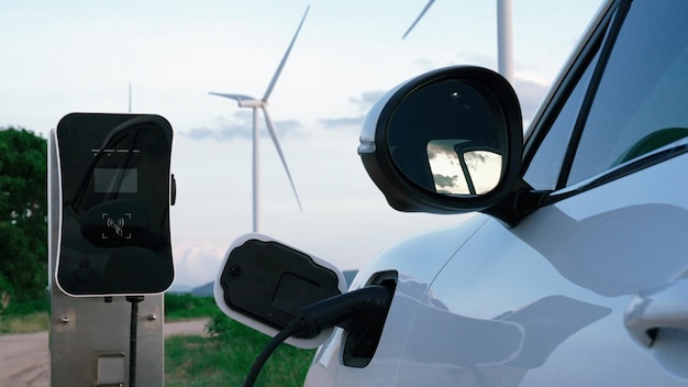 Photo progressive combination of ev car, charging station and wind turbine.