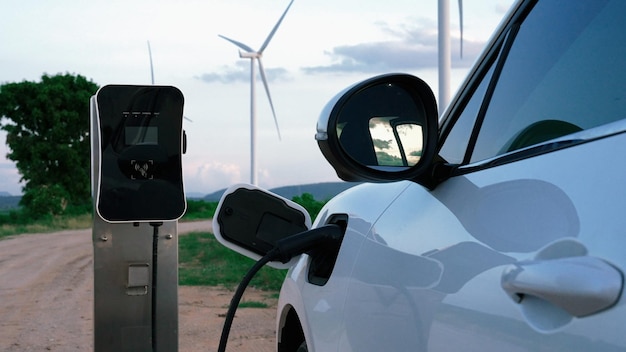 Progressive future energy infrastructure concept of electric vehicle being charged at charging station powered by green and renewable energy from a wind turbine in order to preserve the environment