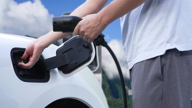 Progressive man recharge electric vehicle installing power cable plug from charging station with rural mountain in the background EV car driven by electro engine for clean environment3