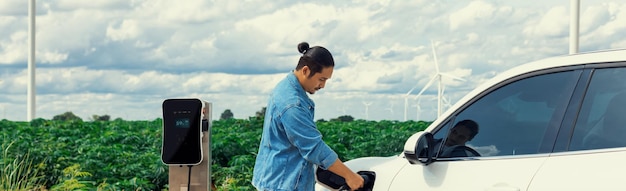 Progressive man with his EV car and wind turbine as concept of renewable energy