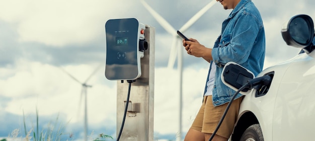 Progressive man with his EV car and wind turbine as concept of renewable energy