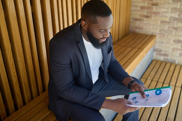 Project documentation. A businessman in a suit sitting on a bench with documents for analyzing in hands