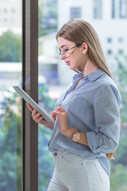 Promising modern young employee is working on a tablet near the window