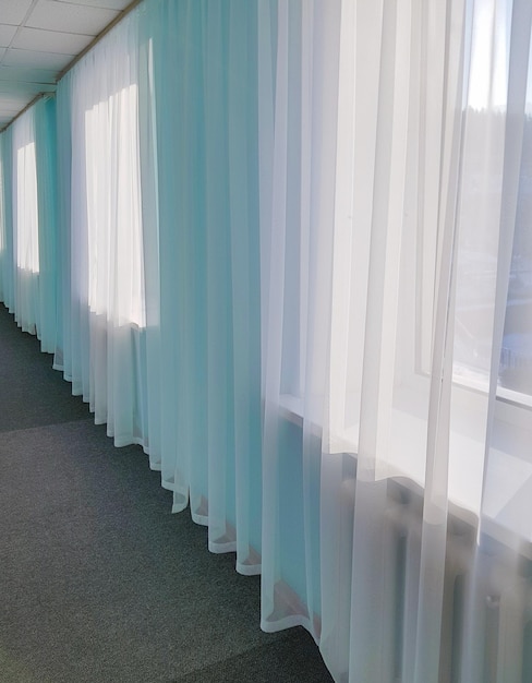 The prospect of a long hotel corridor with transparent curtains on large windows and blue tinting