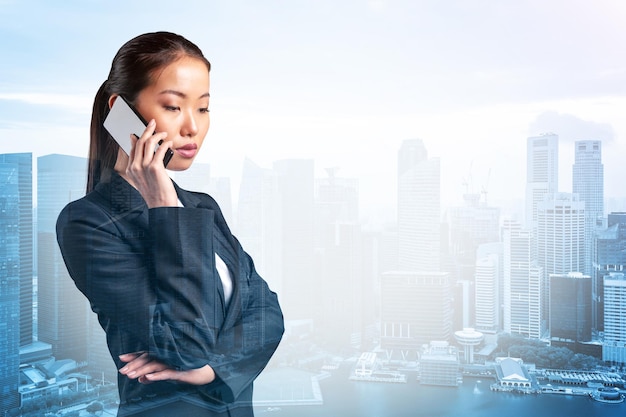 Prosperous astonishing young Asian business woman in suit pensively talking phone Singapore cityscape The concept of consultants as problem solvers Investment fund Double exposure