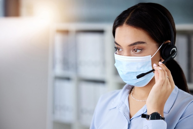 Protecting myself against Covid in the office. Shot of a young call centre agent sitting in the office and wearing a face mask while using her computer.