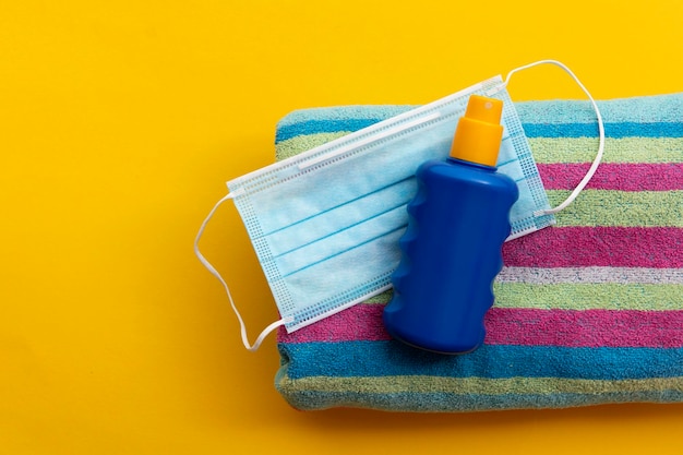 Protective face mask and suncream on a summer vacation beach towel