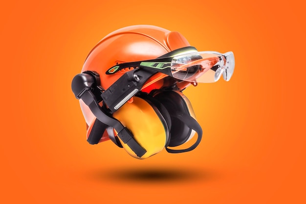 Protective goggles for eyes and construction helmet for head with earmuffs and headlamp on a orange background Construction tool and form for protection