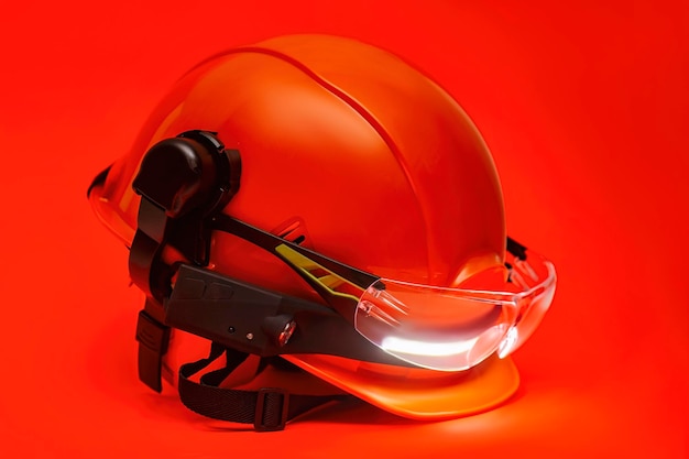 Protective goggles for eyes and construction helmet for head with earmuffs and headlamp on a red background Construction tool and form for protection