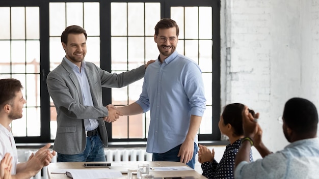 Photo proud boss encouraging and thanking happy employee for good job shaking hand excited worker getting promotion recognition respect and applause of colleagues leader introducing new team member