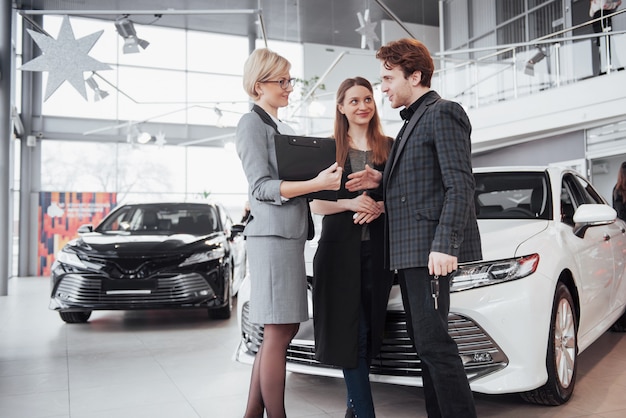 Proud owners. Beautiful young happy couple hugging standing near their newly bought car smiling joyfully showing car keys  copyspace family love relationship lifestyle buying consumerism