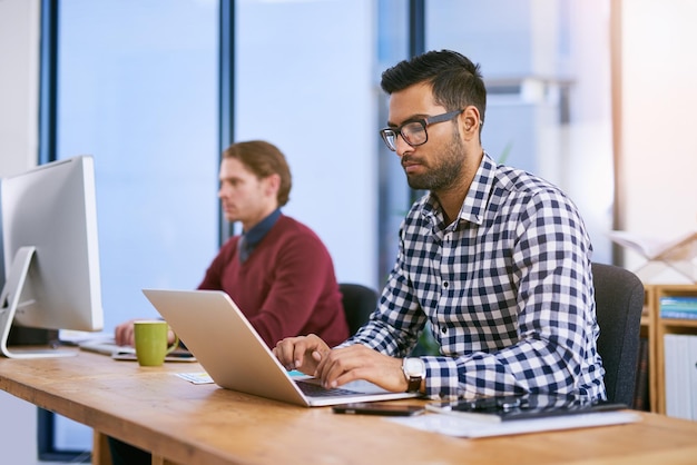 Proving his commitment to the company Shot of a businessman working on his laptop with his colleagues blurred in the background