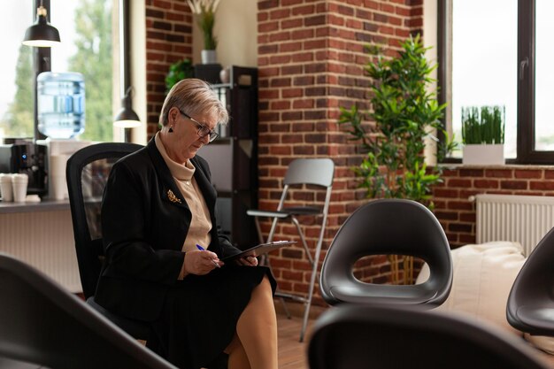 Psychiatrist with clipboard waiting on aa group meeting people, sitting in circle with chairs. Woman therapist preparing for group therapy session with people at rehabilitation office.