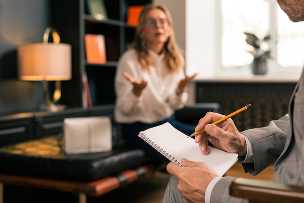 Psychotherapist listening to a female patient while taking notes in his notepad during the session