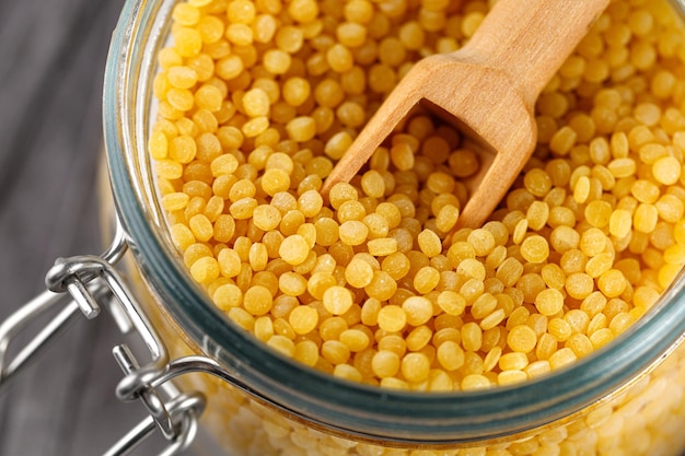 Ptitim Dry uncooked ptitim pasta closeup in a glass jar with spoon Israeli couscous