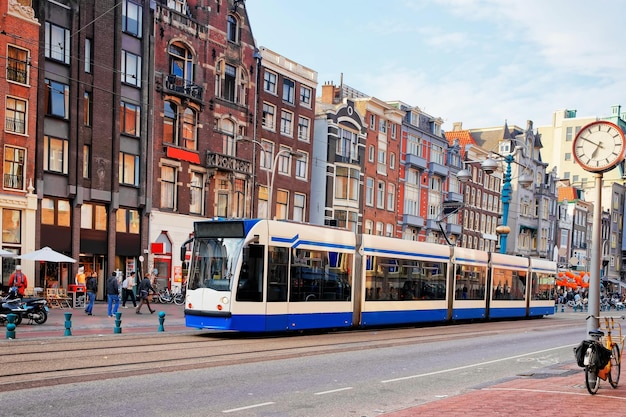 Public tram crossing Damrak main street crowded with tourists in Amsterdam, Netherlands.