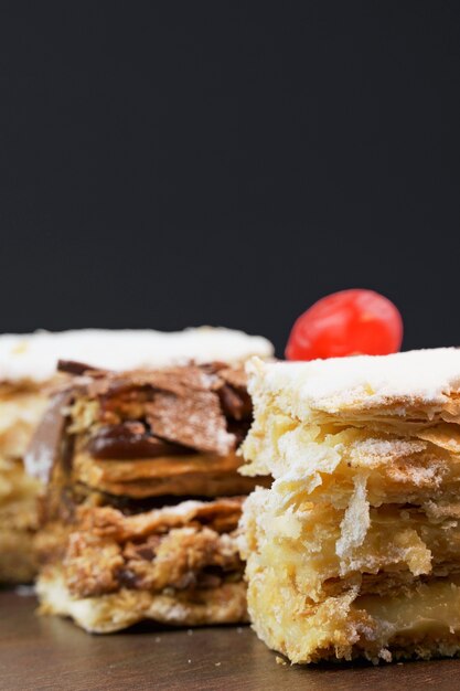 Puff pastry cakes with powdered sugar and cream and another with chocolate and a cherry on top on the wooden table. Close up and space for text. Selective focus. Vertical.