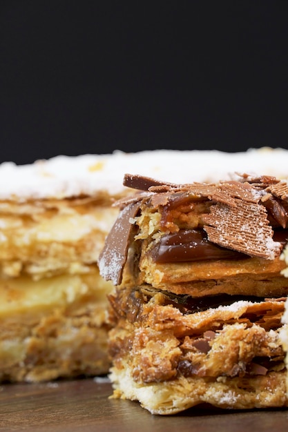 Puff pastry cakes with powdered sugar and cream and another with chocolate and a cherry on top on the wooden table. Close up and space for text. Selective focus. Vertical.