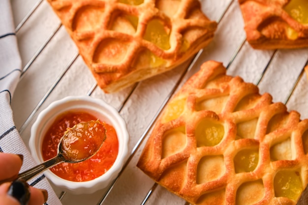 Puff pastry mini pies with pear and lime jam filling on a white plate on on a roasting rack with fresh with pear and lime slices, female hand with a spoon