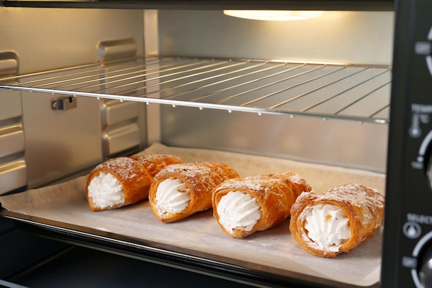 Puff pastry rolls with cream in oven close up