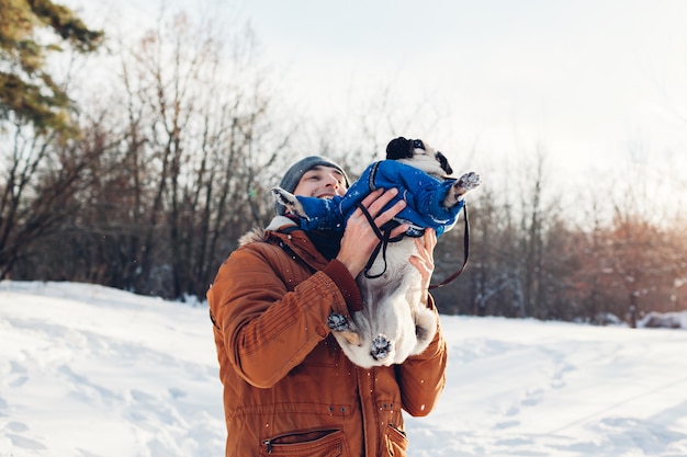 Pug dog walking with his master. Man playing with his pet and having fun. Puppy wearing winter coat.