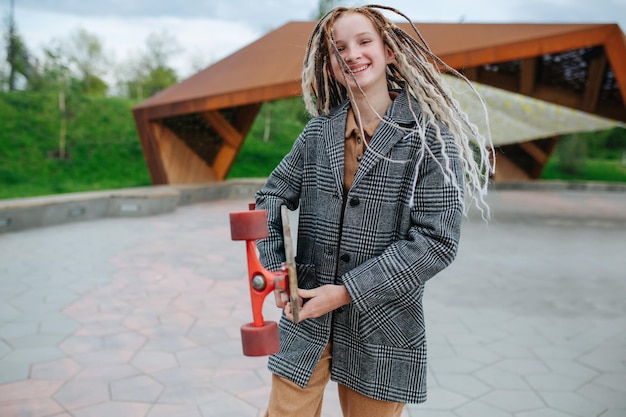 Pumped smiling teenage girl with dreads holding a skate in a park