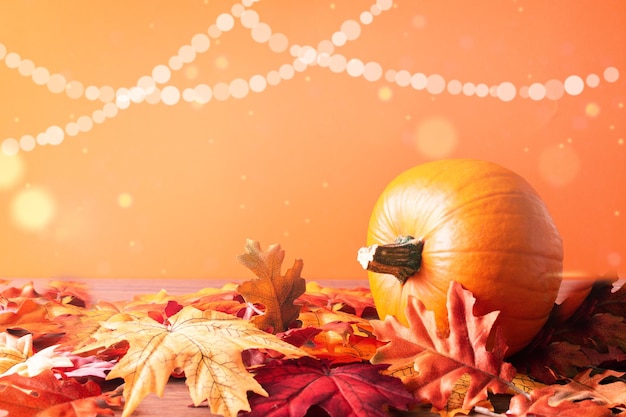 Pumpkin and autumn maple leaves over orange background. Autumn composition