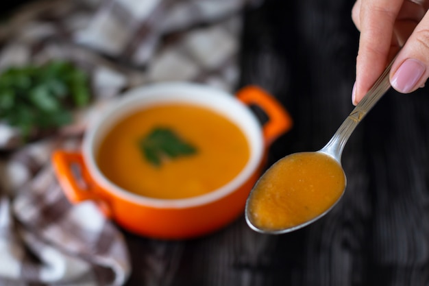 Pumpkin carrot cream soup spoon in an orange plate with cheese pita on a checkered tablecloth 