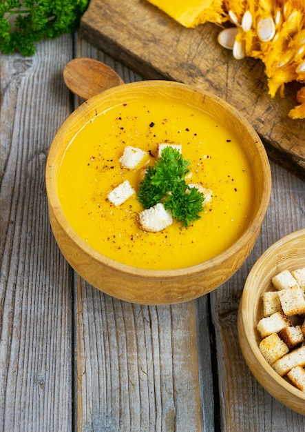 Pumpkin and carrot soup, tadka with cream and parsley on dark wooden table. Top view.