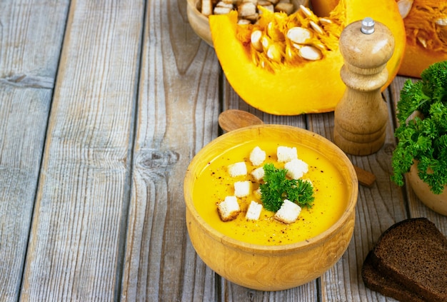 Pumpkin and carrot soup, tadka with cream and parsley on dark wooden table. Top view.