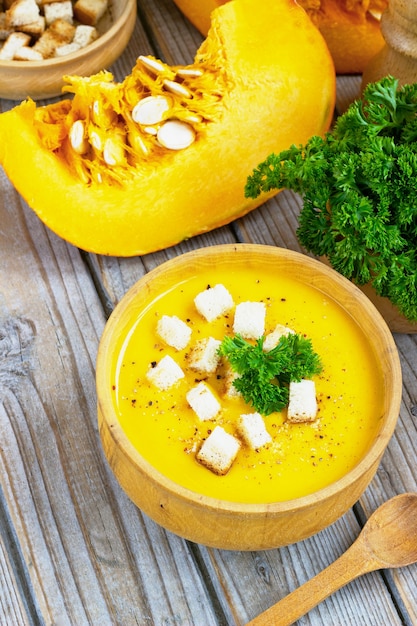 Pumpkin and carrot soup, tadka with cream and parsley on dark wooden table. Top view.