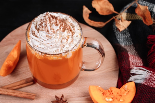 Pumpkin coffee latte with whipped cream on dark background Hot autumn drink with cinnamon and spices in glass mug on a wooden tray