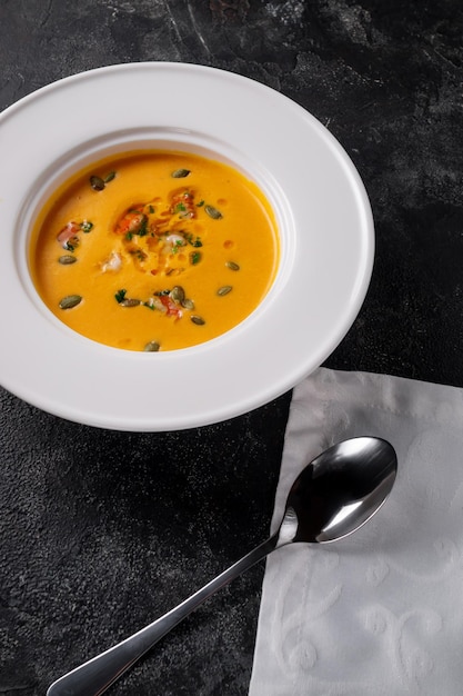 Pumpkin cream soup pureed in a white plate on a dark stone table