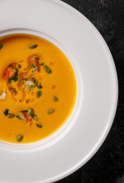 Pumpkin cream soup pureed in a white plate on a dark stone table