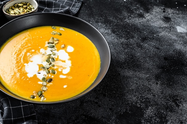 Pumpkin cream soup with cream and pumpkin seeds. black background