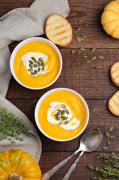 Pumpkin cream soup with cream and pumpkin seeds on old rustic table.