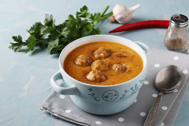 Pumpkin cream soup with meatballs in bowl on light blue surface, Horizontal format, Closeup