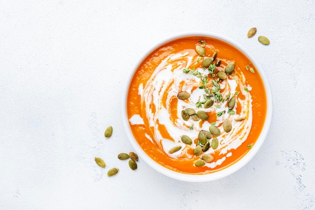 Pumpkin cream soup with pumpkin seeds cream and thyme Winter or autumn healthy vegetarian food White soup bowl on light table background Top view