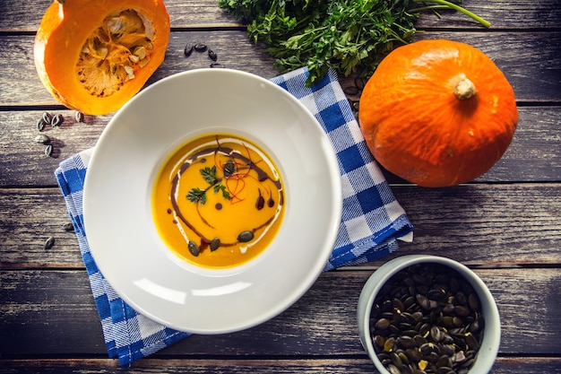 Pumpkin cream soup with seeds and parsley on kitchen table - Top of view.