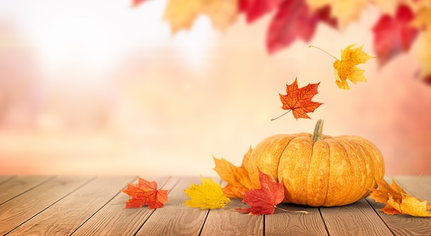 Pumpkin and falling autumn leaves on a wooden table