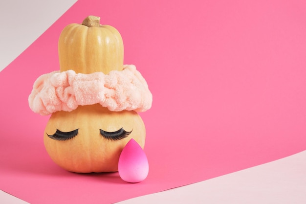 Pumpkin in a headband and false eyelashes on a pink background sponges for applying makeup beauty salon