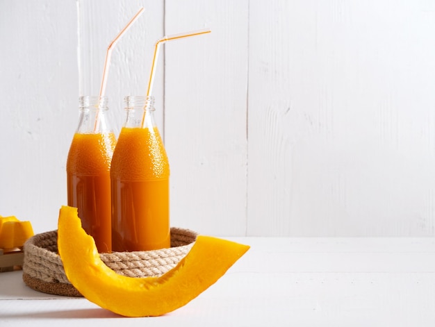 Pumpkin juice in glass bottles on a light background with space for text